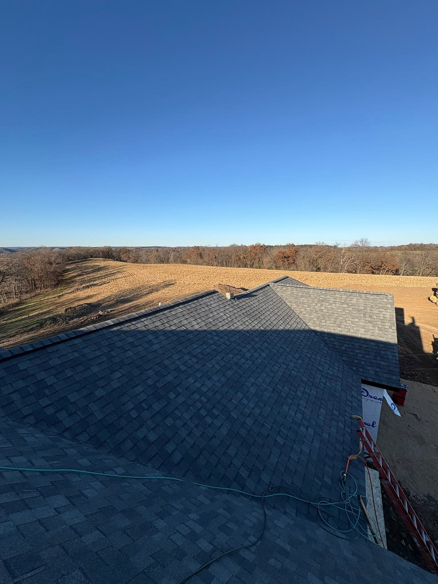 Close aerial view of finished gray roof shingles, ridge caps, and a roof vent