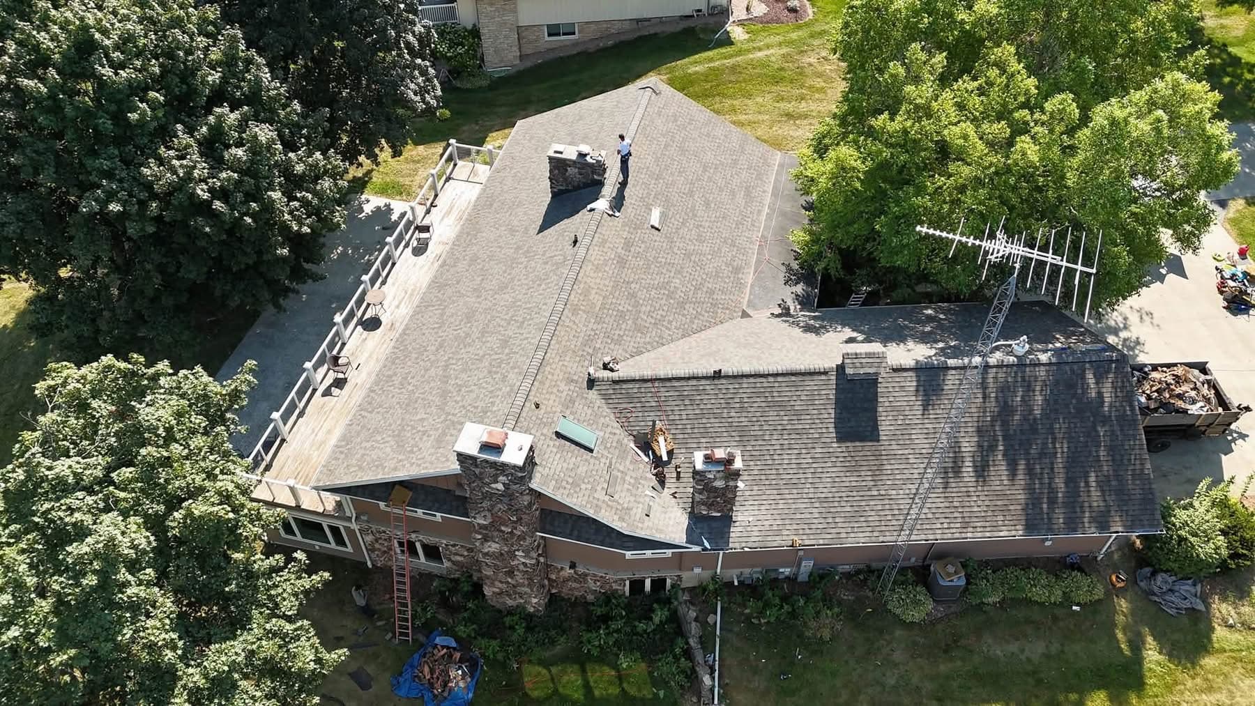 Aerial view of broad installed shingle fields with crew, equipment, ladders, and a debris trailer still present