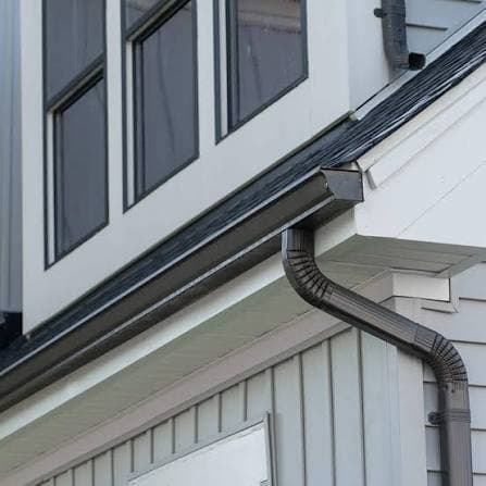 Dark metal gutter and downspout installed along a roofline