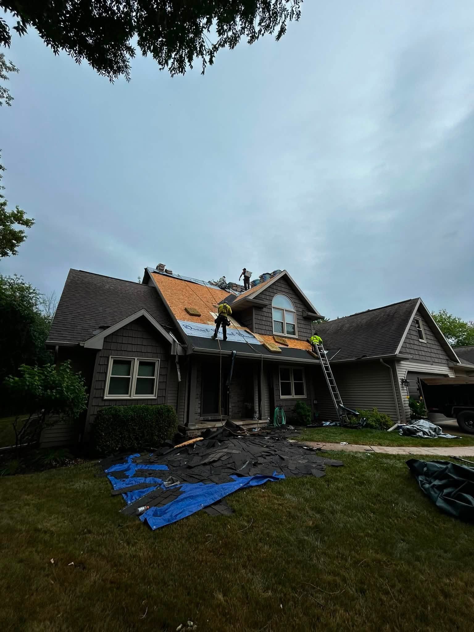 Roofing crew working across partially stripped roof planes during an active residential replacement